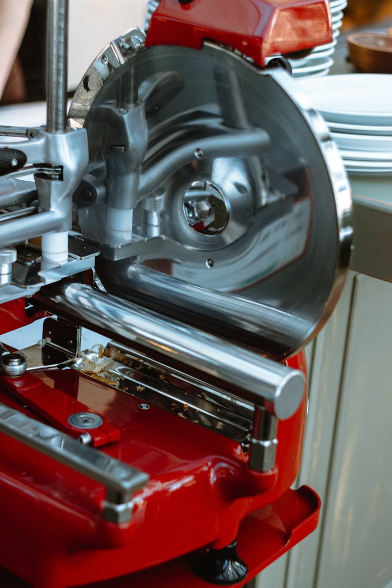 Detailed view of a metallic meat slicer in a kitchen setting, emphasizing its red design and stainless steel blades.
