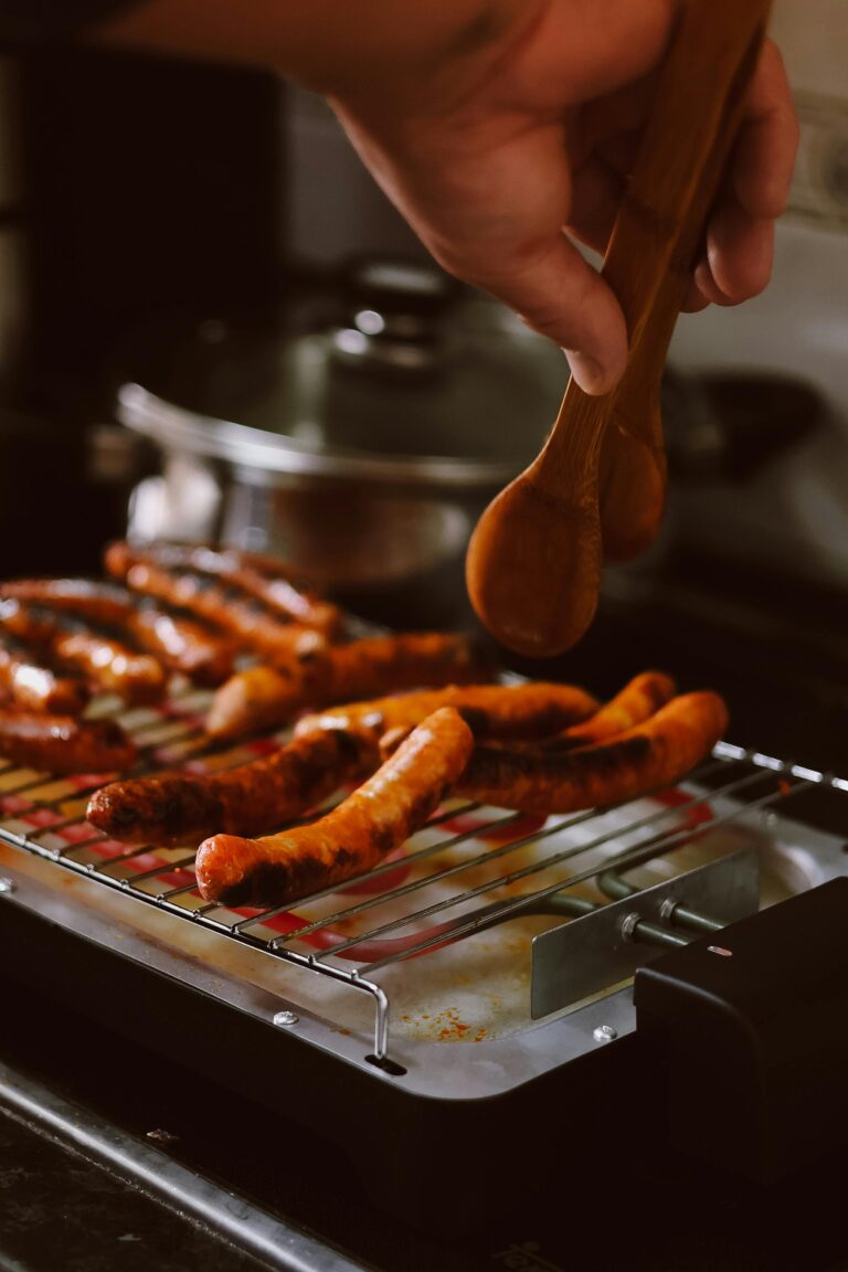 Close-up of sausages being grilled indoors with wooden tongs.
